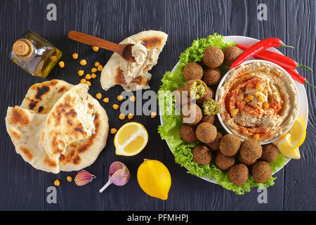Boules de falafel délicieux sur la plaque d'hummus dans un bol, des piments et feuilles de laitue/ pain de pita. L'huile d'olive sur la table en bois noir, authentique destinat Banque D'Images