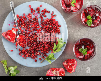 De délicieux jus de grenade froide avec des cubes de glace et de menthe fraîche dans le verre tasses sur table béton frais mûrs avec graines de grenade sur la plaque horizontale, Banque D'Images