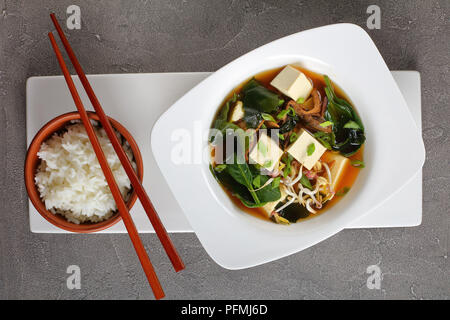 Close-up de la soupe miso servie dans un bol blanc avec des baguettes et du riz vapeur, vue de dessus Banque D'Images