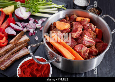 Close-up d'ingrédients bruts pour classic goulasch hongrois - viande de boeuf dans une casserole, paprika, épices et dans des bols, poivron, pomme de terre, oignon, tomate, Banque D'Images