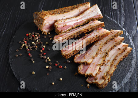 Speck fumé épicé délicieux coupé en tranches sur la plaque en ardoise noire sur la table en bois, vue de dessus, close-up Banque D'Images