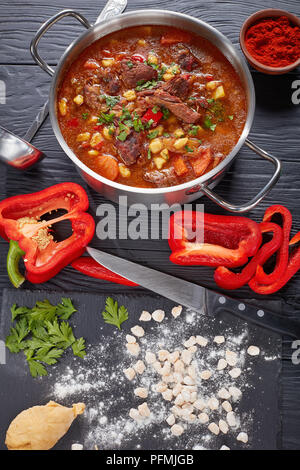 Délicieux chaud goulasch hongrois avec la viande de boeuf, paprika, légumes, dans une casserole. raw csipetke avec la pâte à bord, poivron et une louche sur table, Banque D'Images