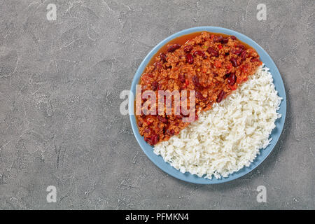 Sex délicieux chili con carne avec des haricots rouges sur la plaque avec du riz bouilli sur table béton, recette classique, vue d'en haut Banque D'Images