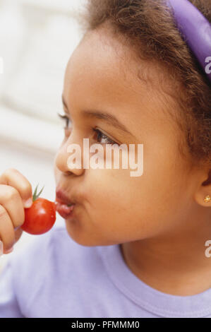 Portrait d'une jeune fille en train de prendre un en-cas dans une vigne, tomate. Banque D'Images