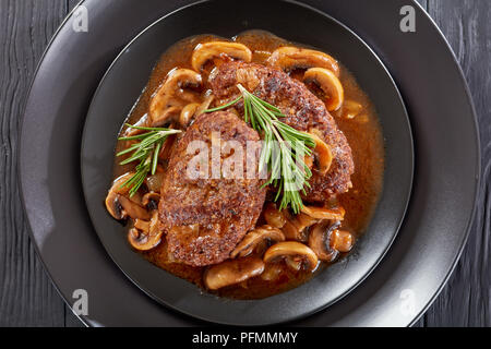 Close-up de partie de sex salé les steaks juteux salisbury avec champignons sauce oignon délicieux servi sur les plaques noires sur la table en bois, vue du dessus Banque D'Images