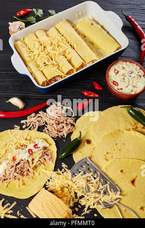 Enchiladas de cuisine fait maison - Tortilla de maïs en couches avec la viande haché, sauce, fromage râpé et des épices dans le plat de cuisson et sur pierre noire, ver Banque D'Images