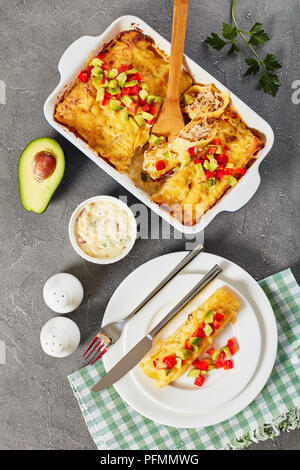 Partie des enchiladas de tortillas de maïs roulées farcies de viande déchiquetée, la sauce, le fromage râpé et les morceaux de piment sur la plaque et dans le plat de cuisson, vue Banque D'Images