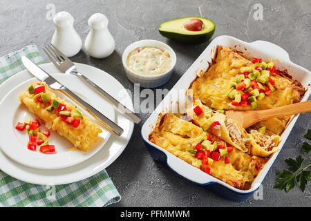 Partie des enchiladas de tortillas de maïs roulées farcies de viande déchiquetée, la sauce, le fromage râpé et les morceaux de piment sur la plaque et dans le plat de cuisson sur con Banque D'Images