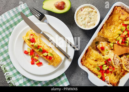 Partie des enchiladas de tortillas de maïs roulées farcies de viande déchiquetée, la sauce, le fromage râpé et les morceaux de piment sur la plaque et dans le plat de cuisson sur con Banque D'Images