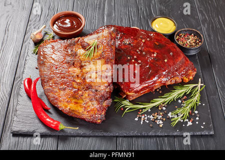 Juteux délicieux barbecue fumé maison côtes levées de porc sur plateau avec pierre noire, d'épices, moutarde et romarin frais sauce bbq, vue de dessus Banque D'Images