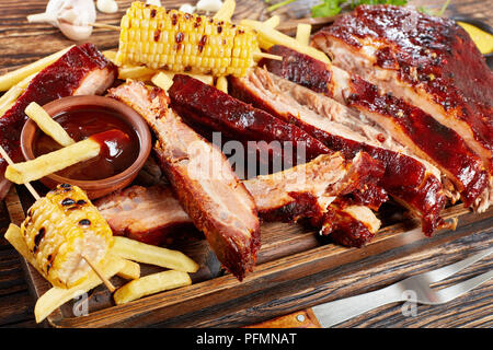 Close-up de juteux délicieux barbecue côtes de porc grillées Maison tomber les os sur planche à découper en bois avec des frites, les épis de maïs grillés, barbe Banque D'Images