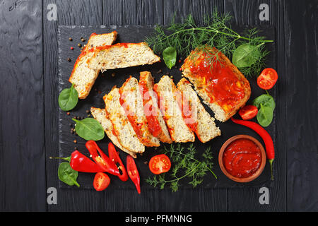 Terrine de poisson délicieux coupé en tranches avec du poivre vert frais, et de la sauce tomate sur l'ardoise noire à découper sur la table en bois sombre, vue d'en haut Banque D'Images