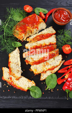 Terrine de poisson au four délicieux coupé en tranches, servi avec des légumes verts, poivre et sauce tomate sur black slate board sur table en bois, vue verticale de Banque D'Images