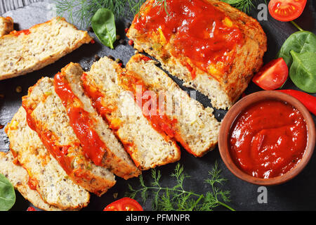 Close-up de terrine de poisson cuit juteux servi avec du poivron rouge, les feuilles d'épinards, tomates cerises et sauce tomate piquante sur black slate board sur bois Banque D'Images