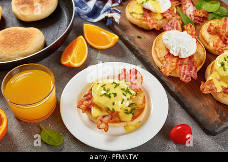 Les oeufs Bénédicte - muffins anglais grillé, frit croustillant de bacon, œufs pochés et sauce hollandaise au beurre classique servi avec du jus d'orange pour le petit déjeuner Banque D'Images