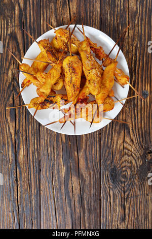 Satay de poulet sur les brochettes sur une plaque blanche sur table en bois rustique, de l'alimentation de rue, recette authentique, vertical Vue de dessus Banque D'Images