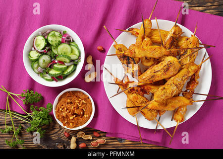 Satay de poulet sur les brochettes sur une plaque blanche sur table en bois rustique servi avec sauce aux cacahuètes et au concombre Salade d'oignons, recette authentique, vue d'en haut, Banque D'Images