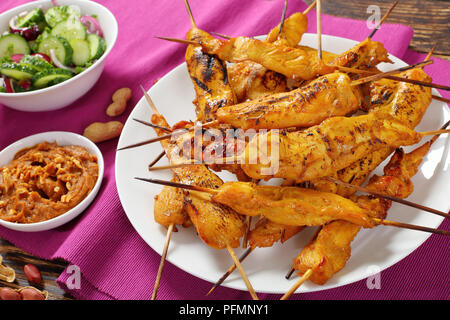 Satay de poulet sur les brochettes sur une plaque blanche sur table en bois rustique servi avec sauce aux cacahuètes et au concombre Salade d'oignons, recette authentique, vue d'en haut, Banque D'Images