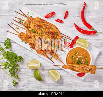 Satay de poulet sur les brochettes, saupoudrée de persil finement haché sur une plaque rectangulaire blanche, sauce aux arachides. piment rouge, tranches de lime et pars Banque D'Images