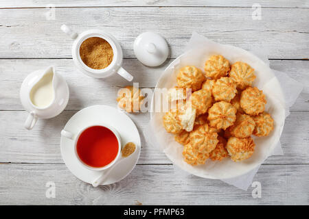 Des délicieux cookies à la noix de coco sur une plaque blanche sur table en bois avec tasse de thé, la cuvette et la crème fraîche dans un pot à lait à l'arrière-plan, vue depuis Banque D'Images