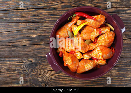 Pilons de poulet cru mariné frotté avec la spice, morceaux de piment, les feuilles de laurier prêt à cuire dans un plat, vue de dessus, l' Banque D'Images