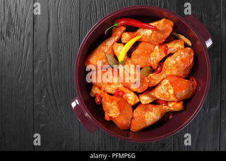 Pilons de poulet cru mariné frotté avec la spice, morceaux de piment, les feuilles de laurier prêt à rôtir dans un plat, vue de dessus Banque D'Images