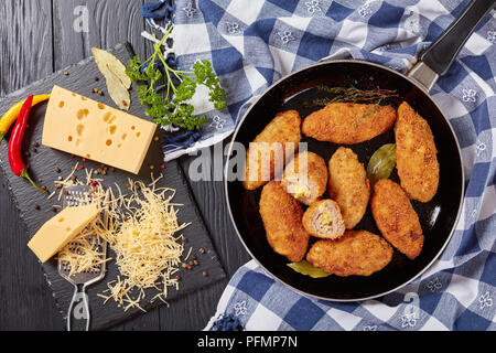 Croquettes de viande pané frit au fromage fondu garniture sur une poêle sur une table en bois avec des ingrédients sur une planche à découper, vue d'en haut Banque D'Images