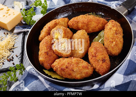 Croquettes de viande pané frit au fromage fondu garniture sur une poêle sur une table en bois avec des ingrédients sur une planche à découper, vue horizontale à partir de ci-dessus, Banque D'Images