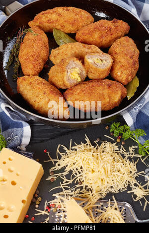 Croquettes de viande panée juteux frits au fromage fondu garniture sur une poêle sur une table en bois avec des ingrédients à l'arrière-plan, vue verticale d'en haut Banque D'Images