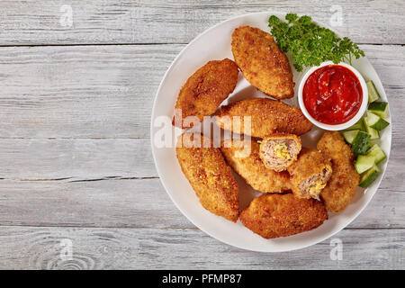 Panés frits croquettes de viande juteuse avec fromage fondu garniture sur une assiette blanche avec salade de concombre et sauce tomate,, vue de dessus, close-up, Banque D'Images