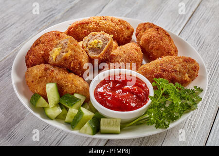 Panés frits juteux des croquettes de viande au fromage fondu garniture sur une assiette blanche avec salade de concombre et la sauce tomate, la vue de dessus, à proximité- Banque D'Images