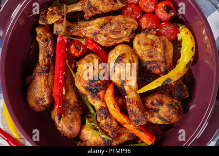 Délicieux pilons de poulet carbonisé multicolores avec des piments et tomates cerises rôties dans brazier, vue de dessus, close-up Banque D'Images