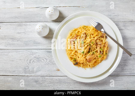 Portion de pâtes, - Tetrazzini à la crème, viande de poulet, de fromage fondu, petits pois, champignons en cocotte sur une plaque blanche avec fourche argent classique, am Banque D'Images
