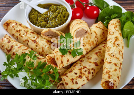 Frites délicieuses crêpes farcies de viande de poulet servi sur une plaque blanche avec épinards, tomates et pesto sauce maison, vue de dessus, close-up Banque D'Images