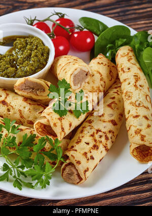 Frites délicieuses crêpes farcies de viande de poulet servi sur une plaque blanche avec des épinards, tomates cerises et sauce maison au pesto, vue de dessus, le clos Banque D'Images