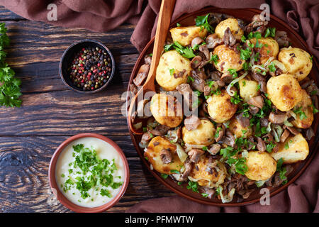 Des pommes de terre nouvelles sautées avec Wild cèpes, oignons et épices sur une assiette avec une cuillère de bois sur une vieille table rustique à la crème, clos Banque D'Images
