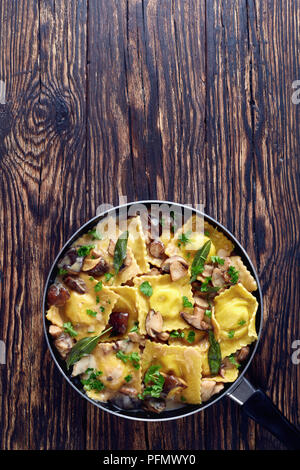 De délicieux ravioli farci de fromage ricotta cuites dans une sauce aux champignons à l'ail crème dans une poêle sur une vieille table en bois, vue du dessus Banque D'Images