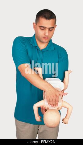 Man holding baby mannequin à l'envers, lui tapotant le dos Banque D'Images