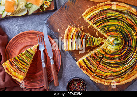 Close-up de tranches de tarte en spirale avec la courgette, l'aubergine, la carotte en lanières de fromage ricotta, servis sur une plaque d'argile avec fourchette et couteau, voir à partir de Banque D'Images