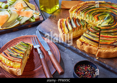 Close-up de tranches de tarte en spirale avec la courgette, l'aubergine, la carotte en lanières de fromage ricotta, servis sur une plaque d'argile avec fourchette et couteau, voir à partir de Banque D'Images