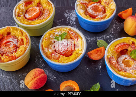 Délicieux dessert d'été français - abricot flaugnarde dans les ramequins sur une plaque en ardoise noire, sur une table en bois, vue de dessus, télévision lay, close-up Banque D'Images