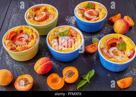 Délicieux dessert d'été français - abricot flaugnarde dans les ramequins sur une plaque en ardoise noire, sur une table en bois, vue de dessus, close-up Banque D'Images