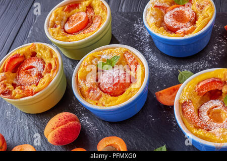 Délicieux dessert d'été français - abricot flaugnarde dans les ramequins sur une plaque en ardoise noire, sur une table en bois, vue de dessus, close-up Banque D'Images