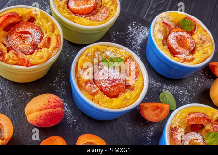 Délicieux dessert d'été français - abricot flaugnarde dans les ramequins sur une plaque en ardoise noire, sur une table en bois, vue de dessus, close-up Banque D'Images