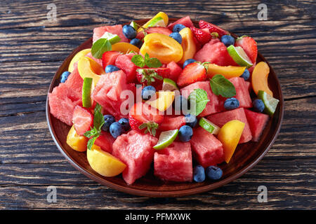 De délicieux produits frais colorés avec des bleuets, salade de pastèque tranches de pêches, de fraises et citron vert sur une plaque d'argile sur une vieille table rustique, vue horizontale Banque D'Images