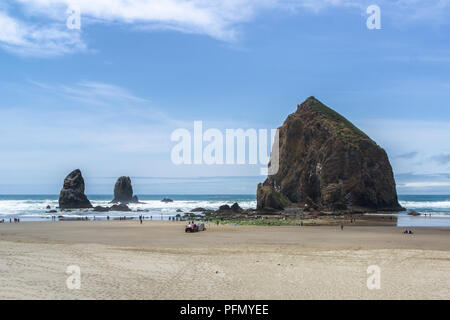 La Haystack Rock Wildlife Refuge avec les personnes bénéficiant des flaques à marée basse, Cannon Beach, côte de l'Oregon, USA. Banque D'Images