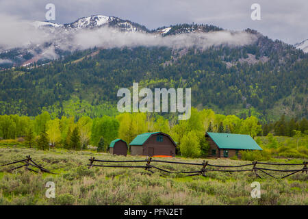 Belle vue extérieure de maisons en bois avec toit vert brun situé dans la vallée de lamar dans le Parc National de Yellowstone (Wyoming) avec une montagne derrière, couvertes de neige partielle Banque D'Images