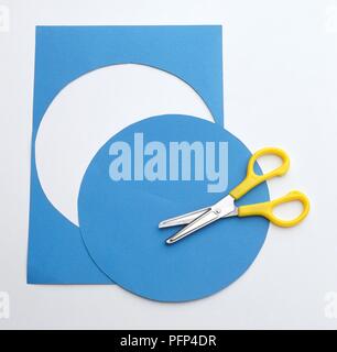 Cercle coupé de forme oblongue feuille de papier bleu à l'aide de ciseaux jaune Banque D'Images