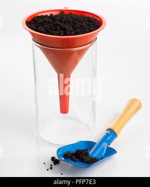 Entonnoir en plastique contenant de la terre placée dans un bécher en verre, certains sur le sol à proximité de la truelle Banque D'Images