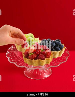 Retrait de la framboise tartelette à couper le verre cakestand Banque D'Images